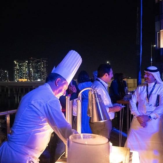 Chef plating at the waterside evening, Abu Dhabi skyline behind