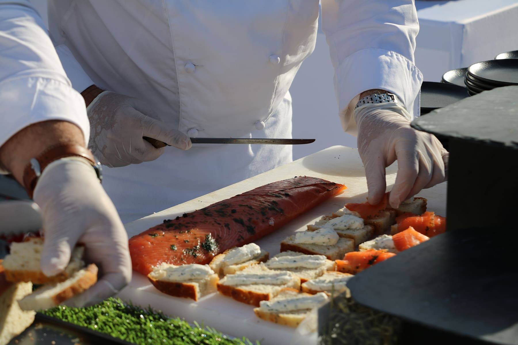 Chef in whites slicing house-cured salmon for canapés at the show-cooking station