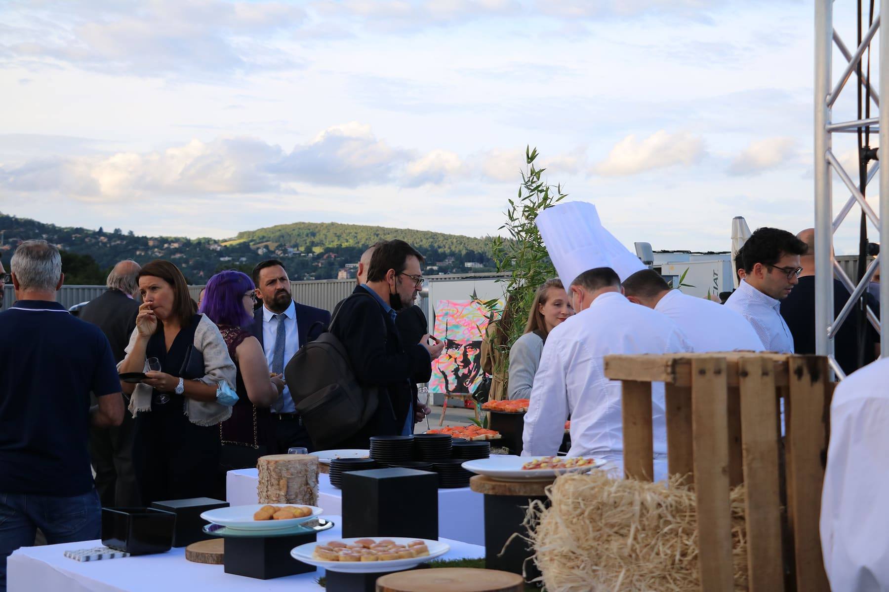 Guests in conversation by the buffet as chefs plate canapés, hills beyond the rooftop