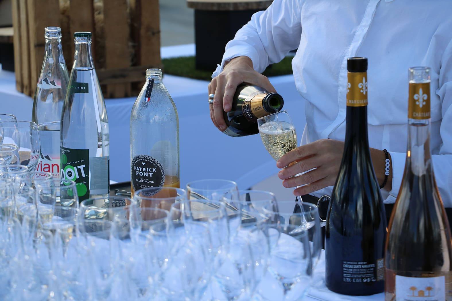 Server pouring sparkling wine into a flute beside Château Sainte-Marguerite bottles