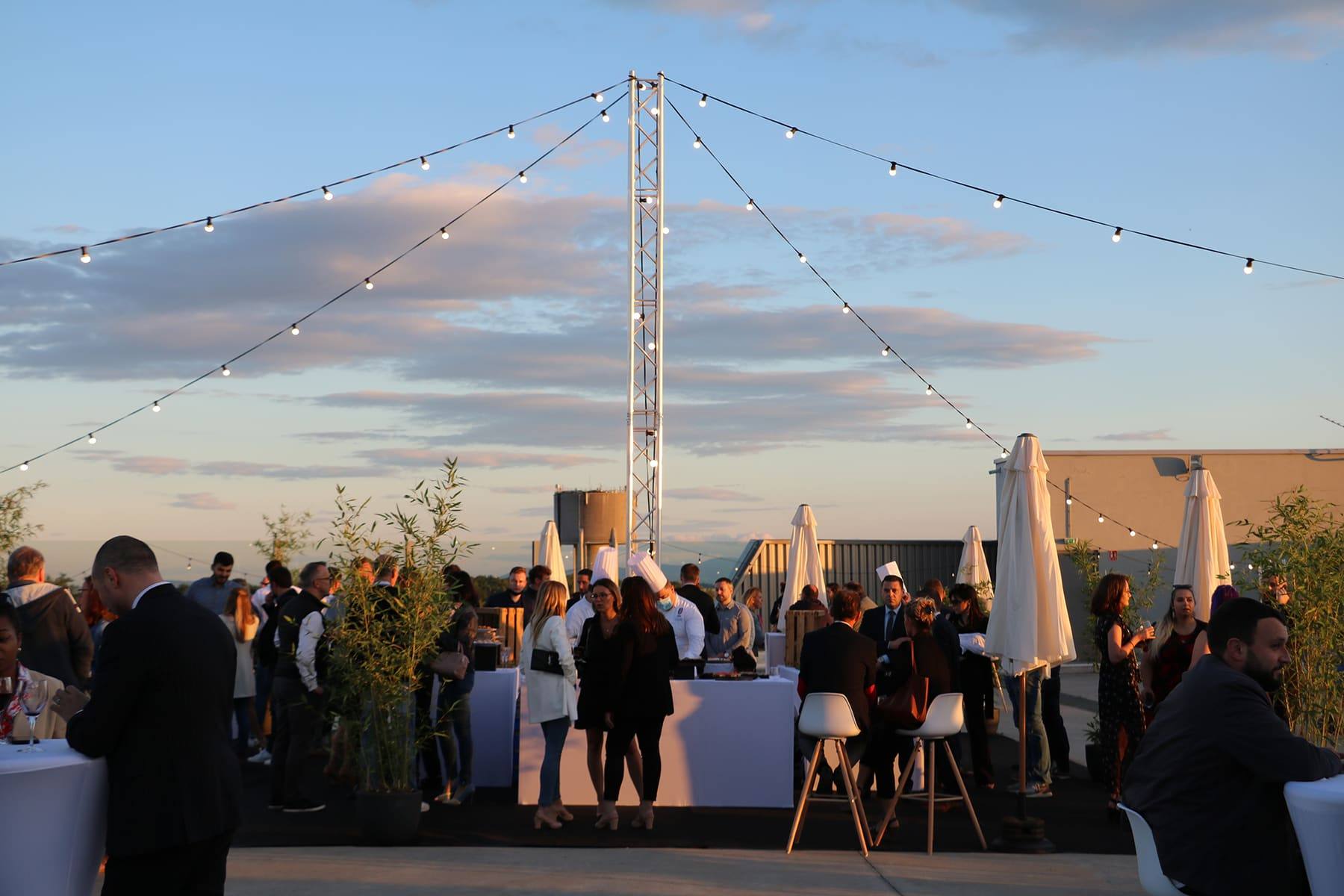 String-lit rooftop terrace at dusk, guests gathered around white cocktail tables