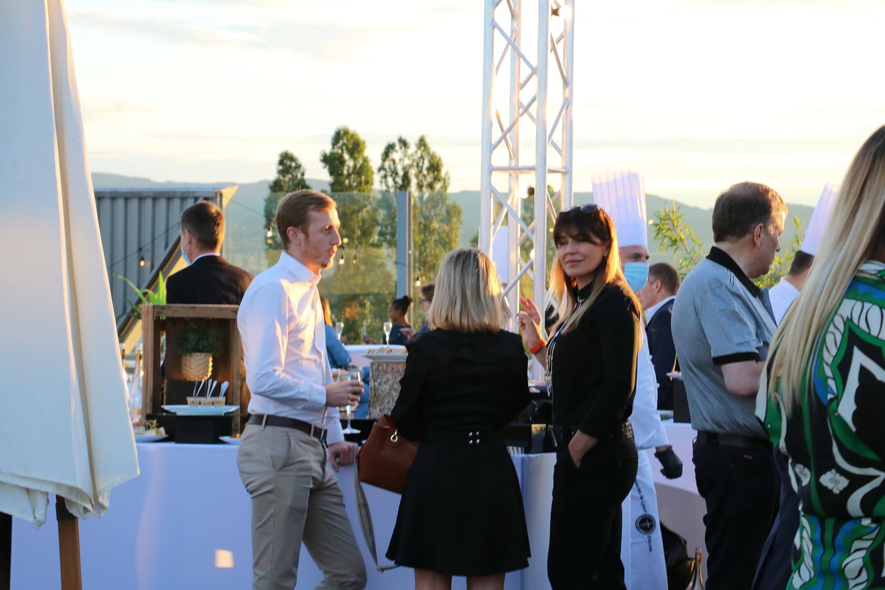 Guests with flutes chatting beside a lighting truss, chef and skyline in the background