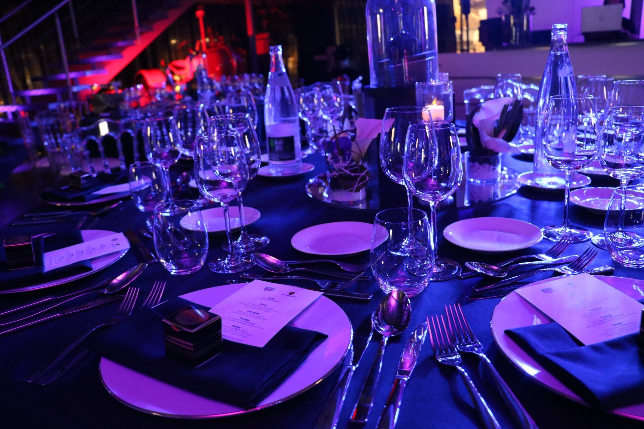 An elegant gala table set under deep blue light at a Table of Taste event