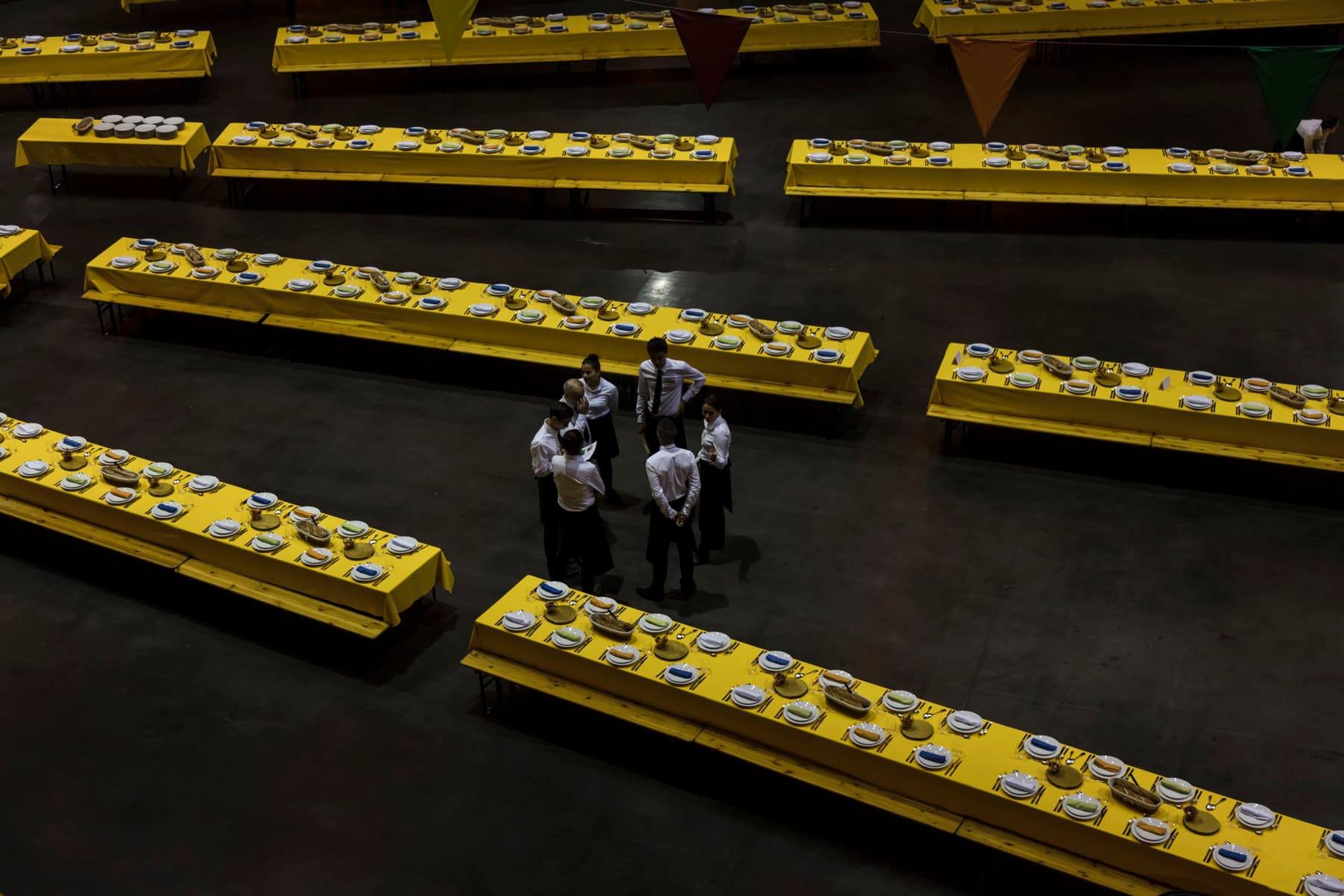 Aerial view of set banquet tables in yellow as waitstaff confer before service