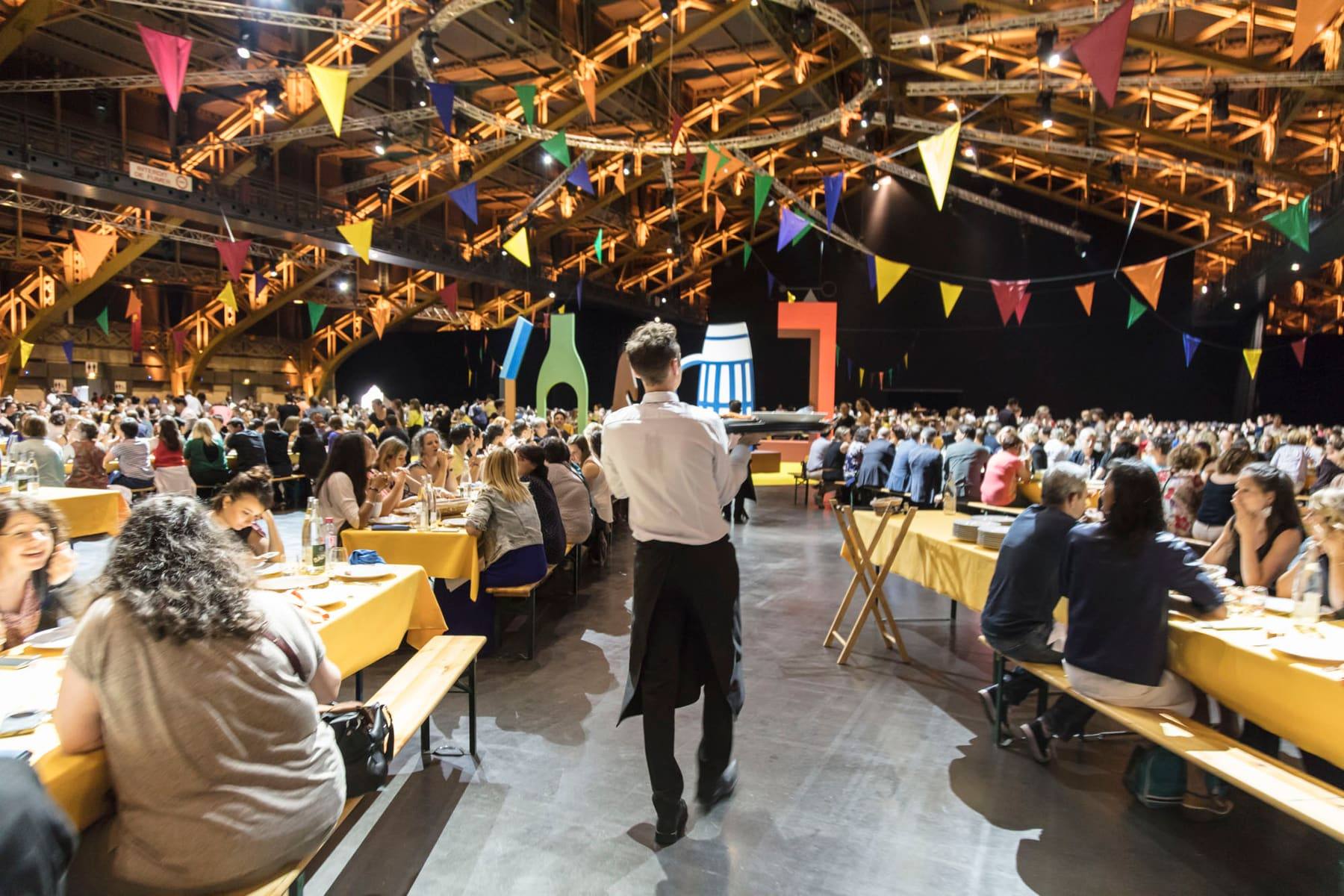 Guests dining at long communal tables beneath festive bunting in the hall