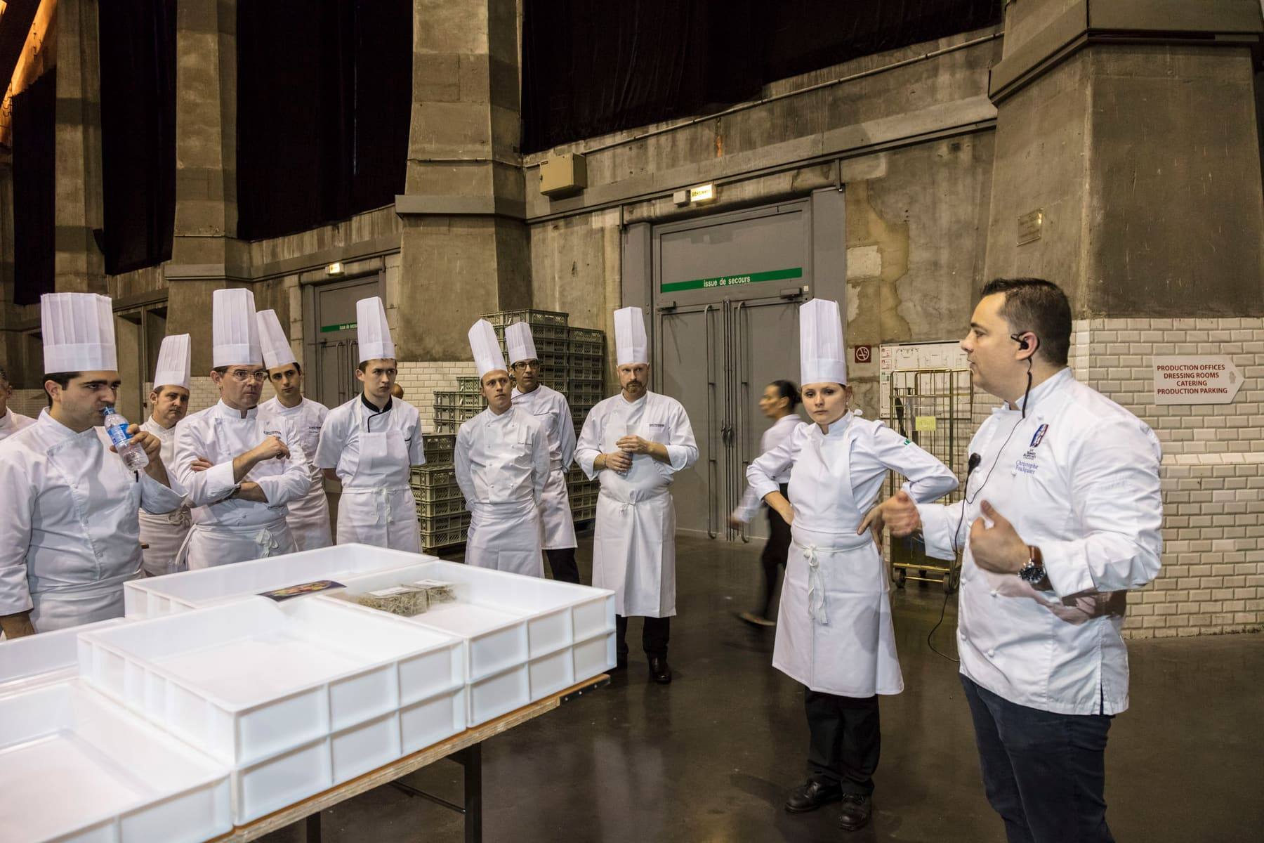 Brigade of chefs in toques gathered for a briefing in the venue's industrial bay