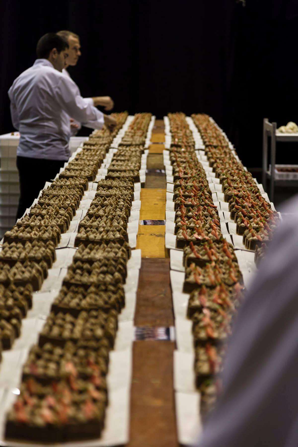Chef in whites arranging hundreds of identical canapés along a long table