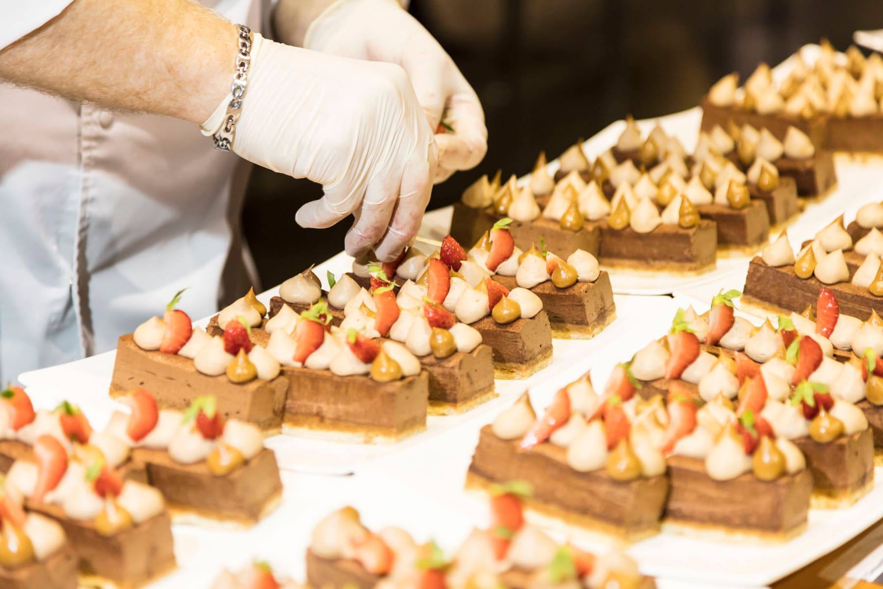 Gloved hand finishing rows of chocolate mousse desserts topped with strawberries