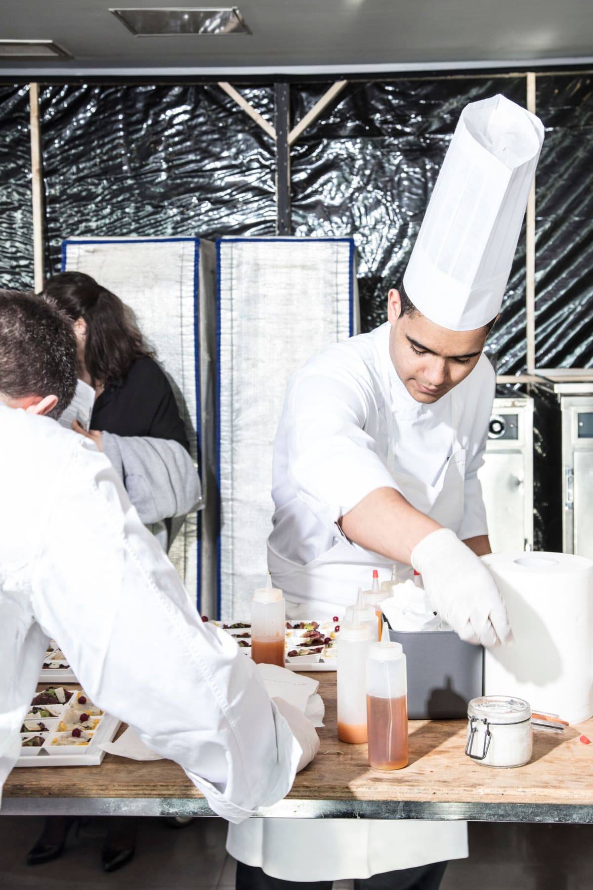 Chef in toque finishing canapés at a live station as guests look on