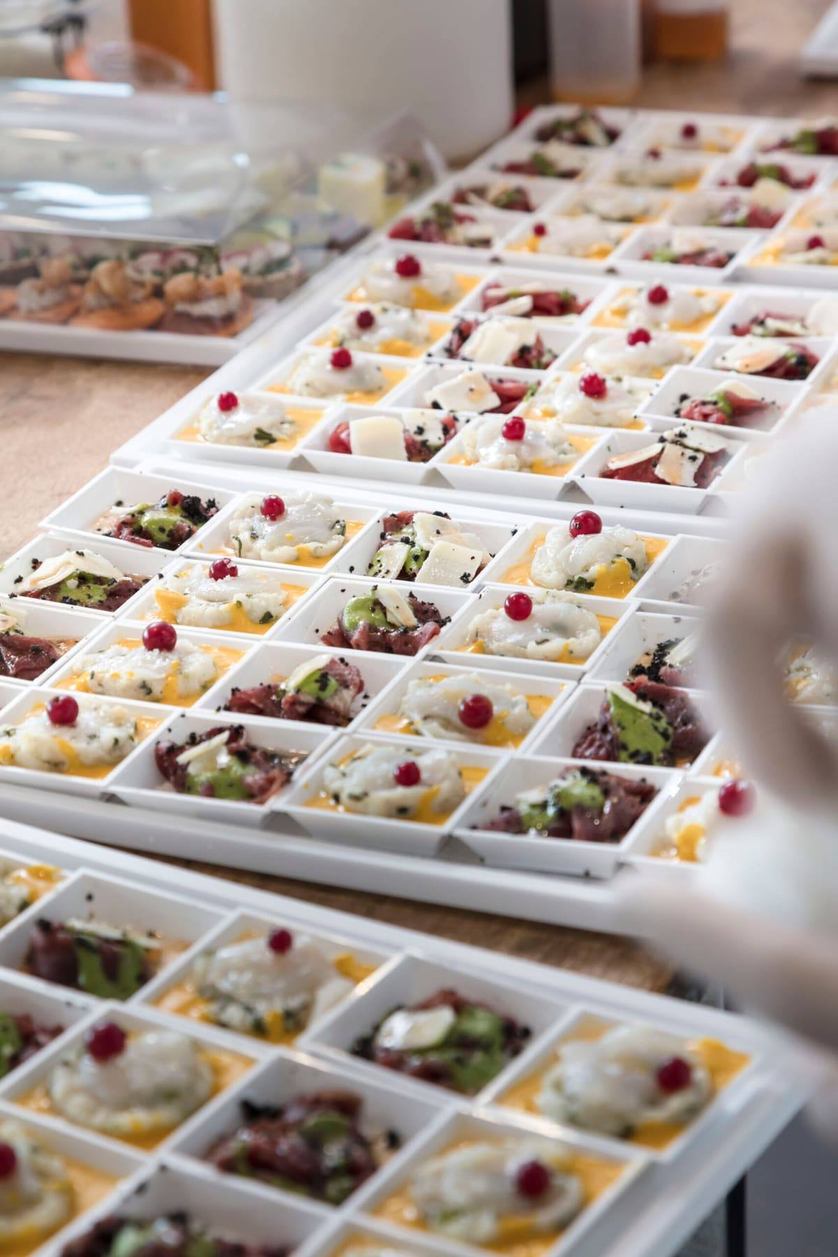 Trays of bite-size tartare verrines garnished with redcurrants on a prep table