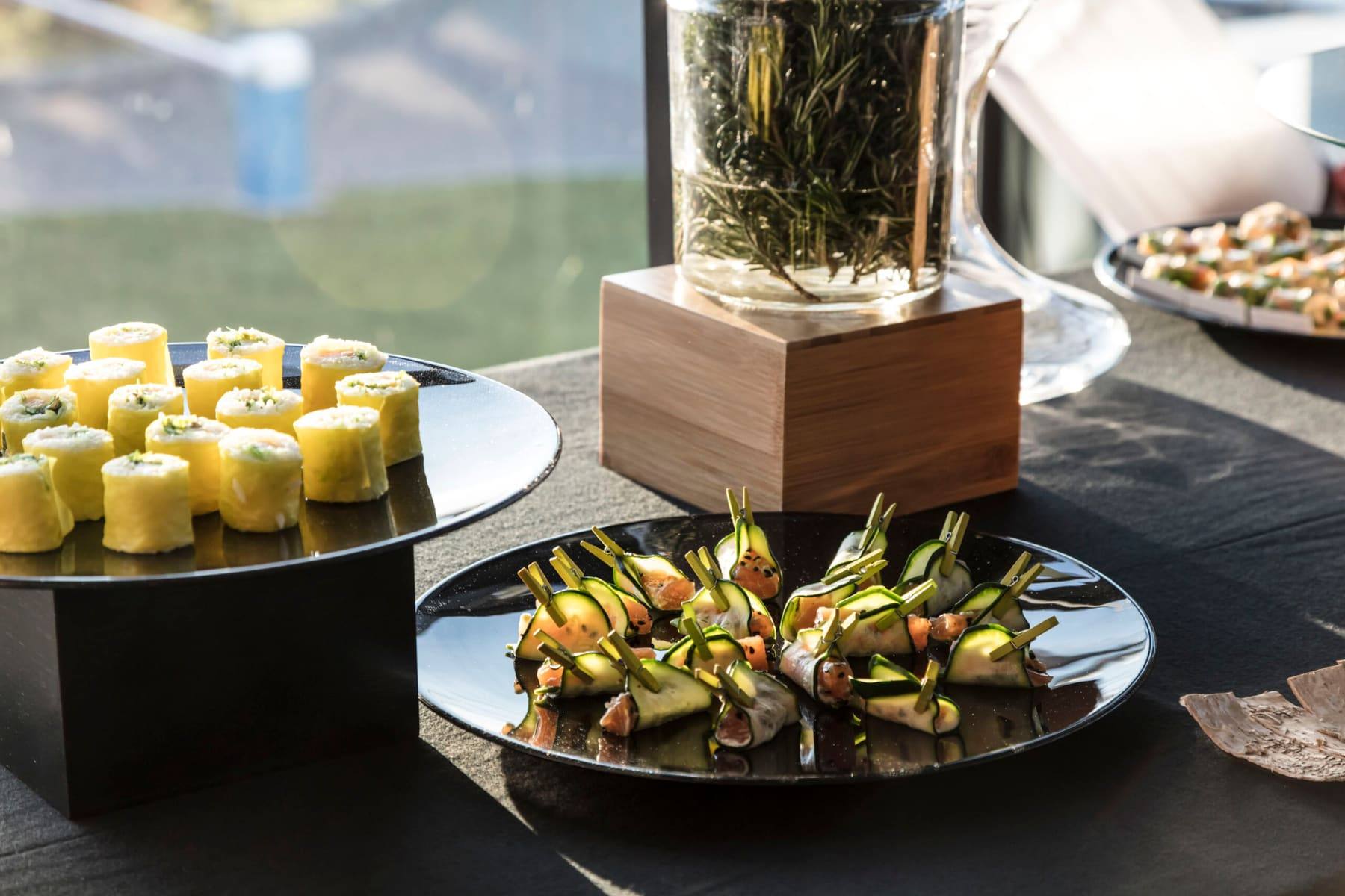 Detail of zucchini-wrapped bites and rolled canapés plated on black slate