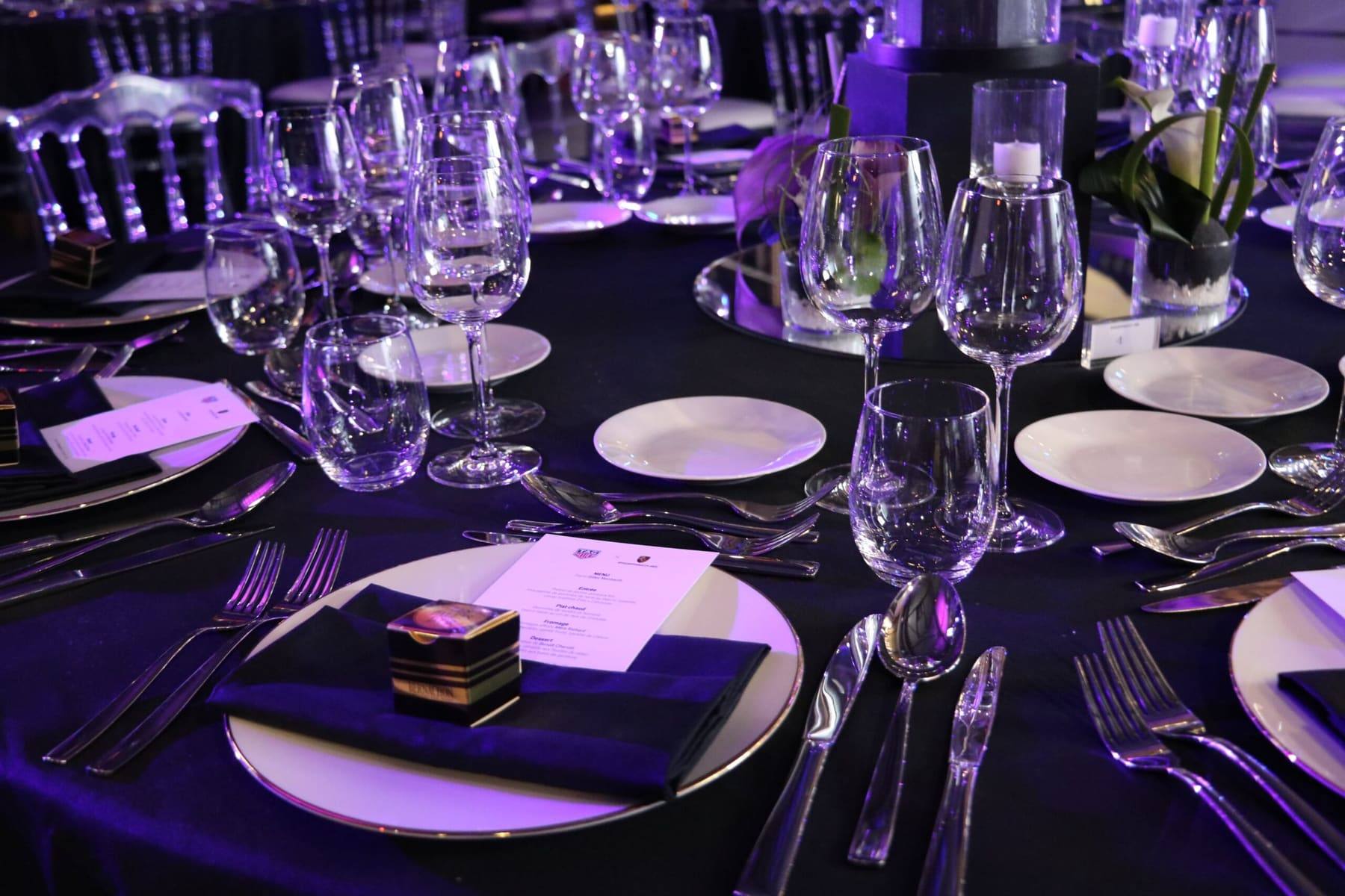 Place setting with menu card, gilt-rimmed plate and crystal glasses under violet lighting