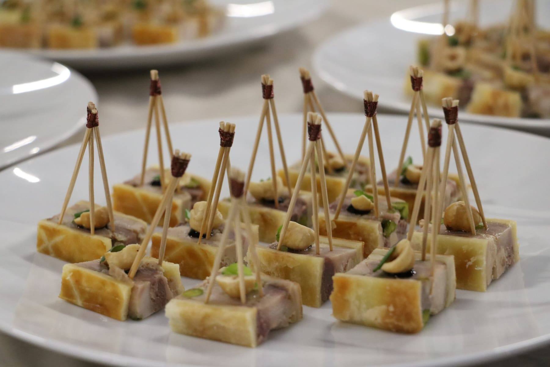 Foie gras terrine bites pinned with wooden picks and cashews on a white plate