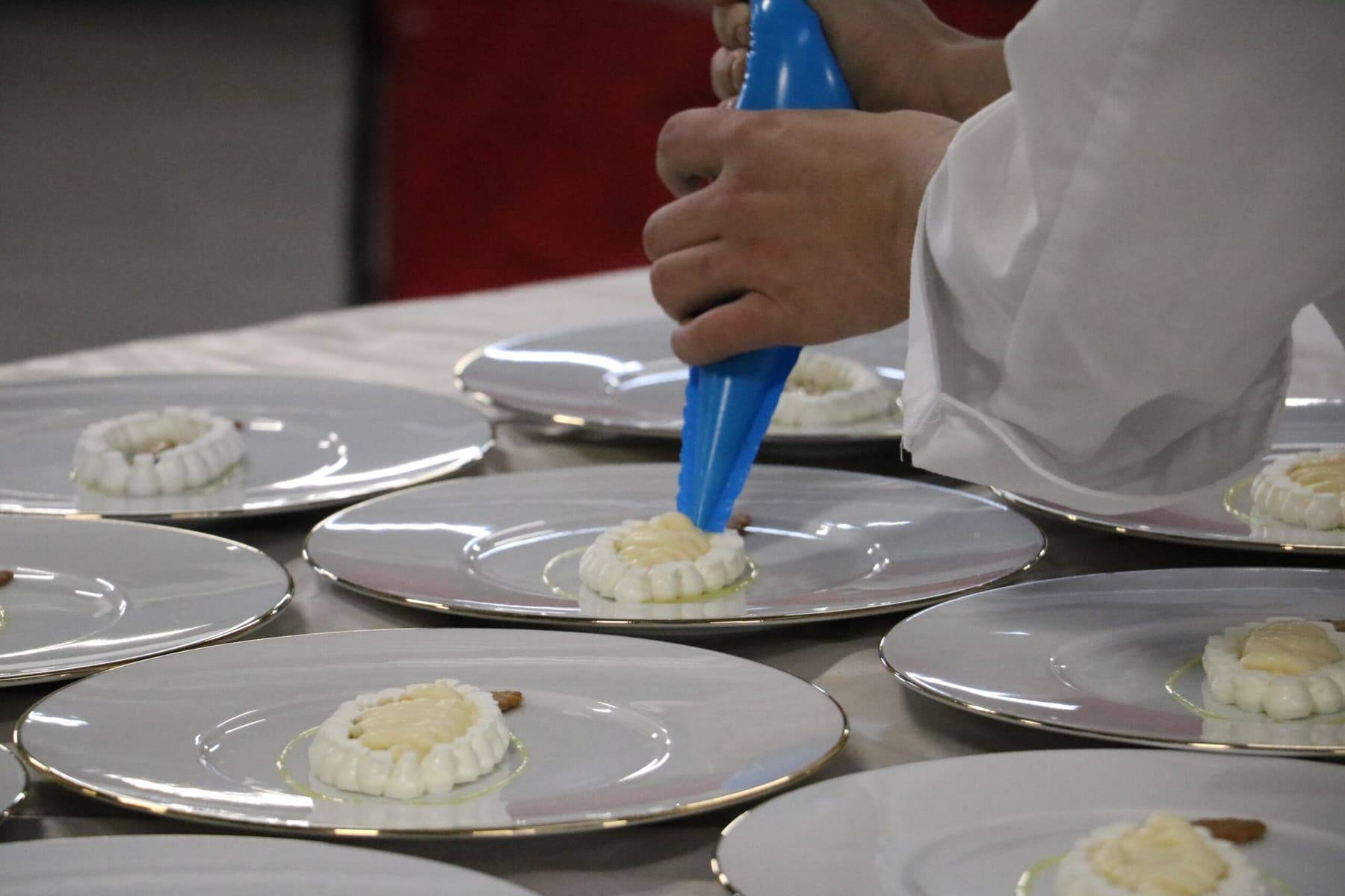 Chef piping cream onto silver-rimmed plates during dessert preparation