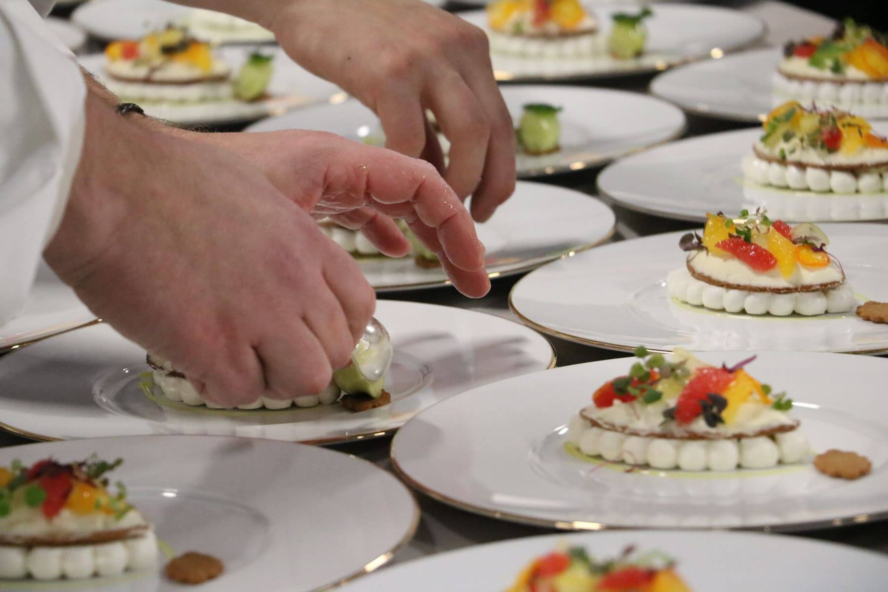Chef finishing fruit desserts with a quenelle, plates laid out across the table
