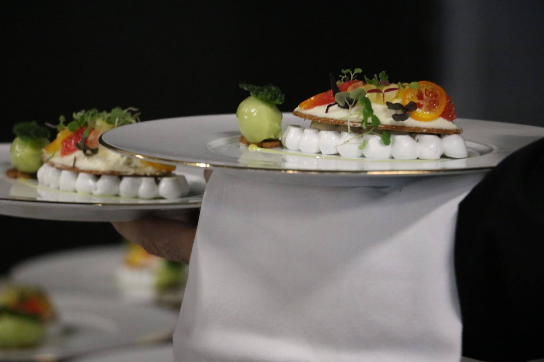 Waiter carrying a tray of citrus desserts topped with microgreens through the room